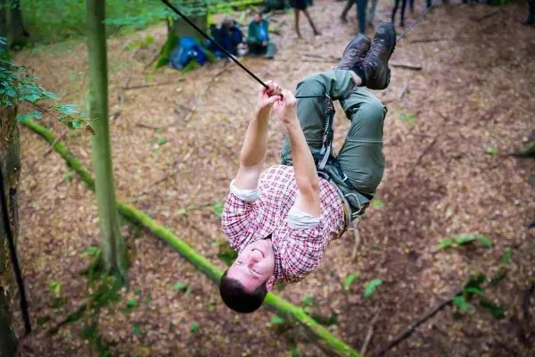 Seilquerung mit Karabiner in einem Waldgebiet, Person hängt kopfüber