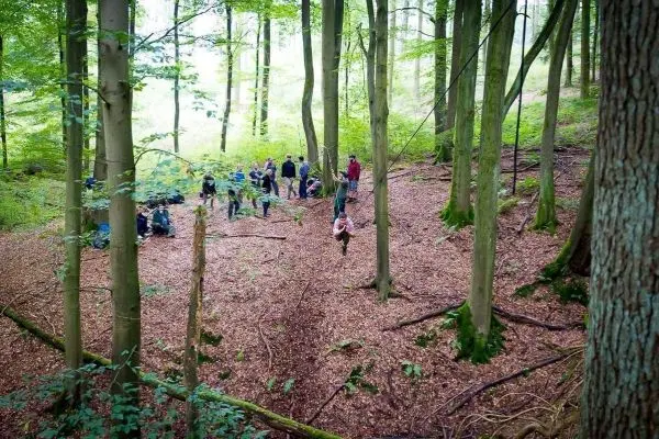 Selbstgebaute Seilquerung zwischen Bäumen, Teilnehmer stehen im Hintergrund auf Laub