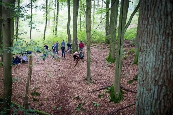Teilnehmer überqueren eine selbstgebaute Seilbrücke zwischen Bäumen im Wald