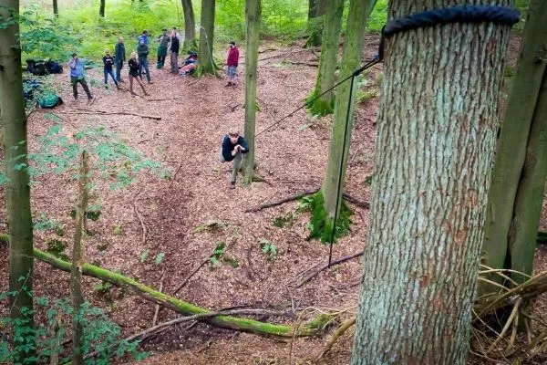 Teilnehmer überqueren eine selbstgebaute Seilbrücke zwischen zwei Bäumen