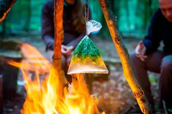 Tüte mit Lebensmitteln hängt über dem Feuer beim Kochen im Freien