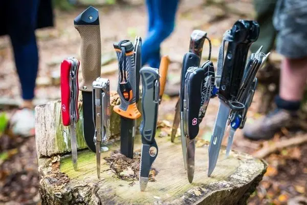 Verschiedene Messer und Multitools stehen auf einem Baumstumpf im Wald