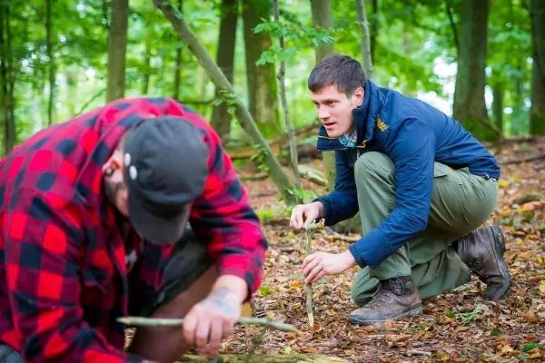 Zwei Personen arbeiten im Wald mit Holzstöcken und bereiten eine Technik vor