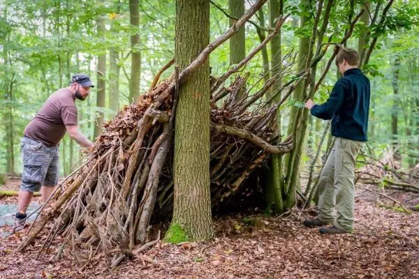Zwei Personen bauen eine improvisierte Notunterkunft aus Ästen und Laub