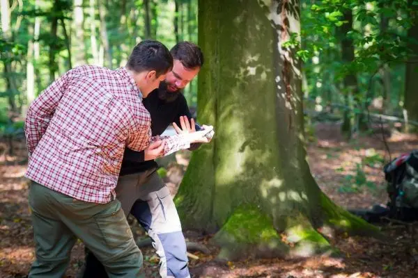 Zwei Personen betrachten eine Karte vor einem Baum im Wald