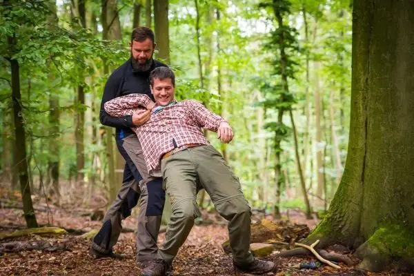 Zwei Personen führen eine improvisierte Tragehilfe im Wald durch