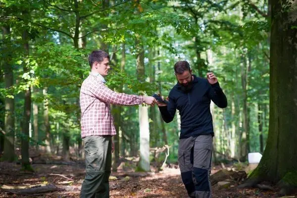 Zwei Personen führen eine Übergabe eines Gegenstands im Wald durch