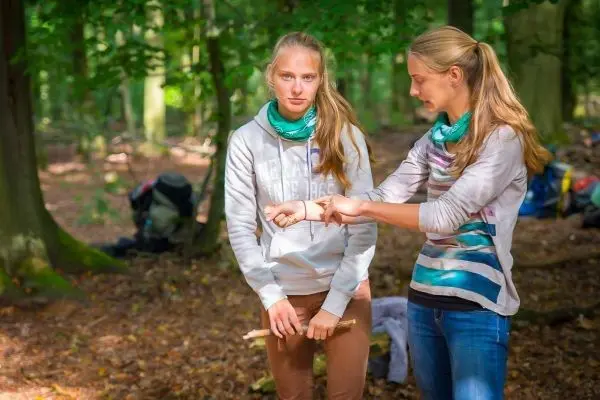 Zwei Personen im Wald, eine hält einen Stock und zeigt eine Technik
