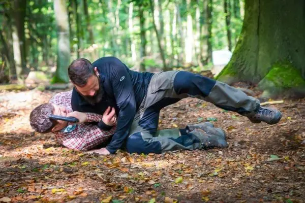 Zwei Personen im Wald, eine Person kontrolliert die andere am Boden