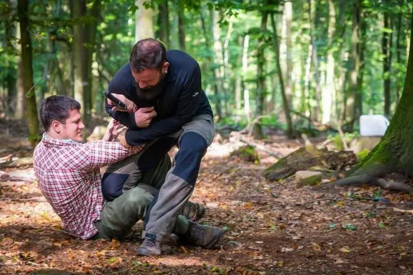 Zwei Personen kämpfen am Boden im Wald, einer hält den anderen fest