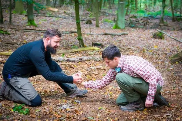 Zwei Personen knien im Wald und arbeiten gemeinsam an einem Feuerstarter