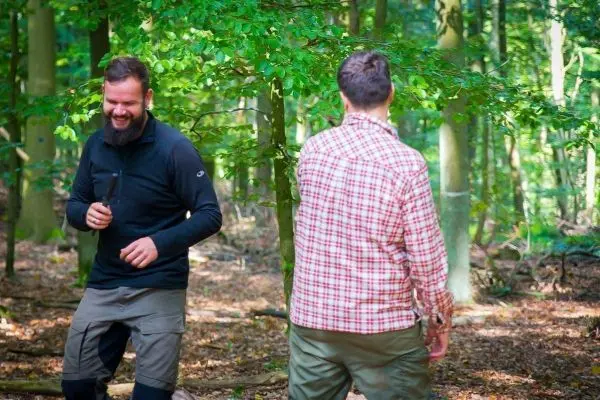 Zwei Personen lachen und bewegen sich im Wald zwischen Bäumen
