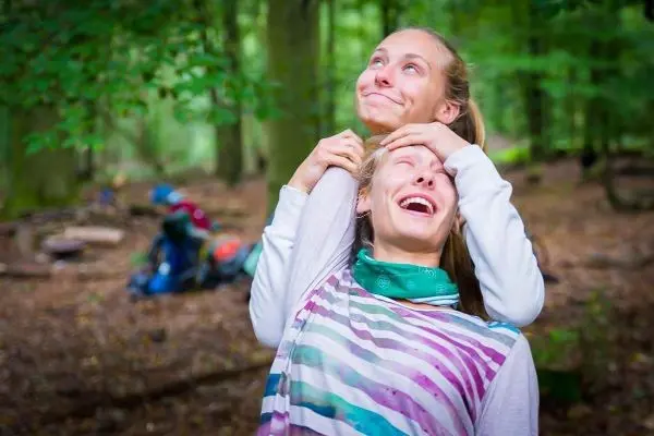 Zwei Personen lachen und posieren im Wald, Rucksäcke im Hintergrund