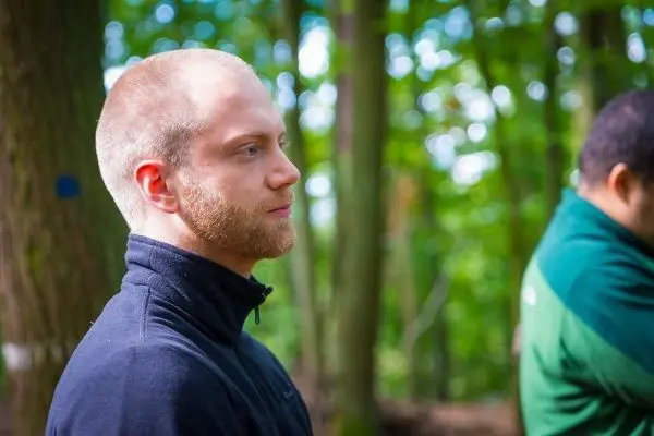 Zwei Personen stehen im Wald, eine Person schaut nachdenklich zur Seite