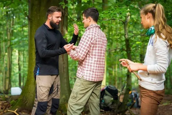 Zwei Personen stehen im Wald und diskutieren, während eine dritte Person beobachtet