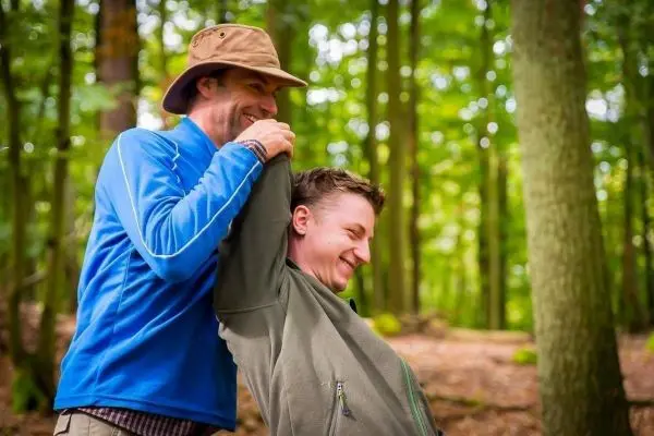 Zwei Personen stehen im Wald und lachen, einer hält den anderen am Kragen