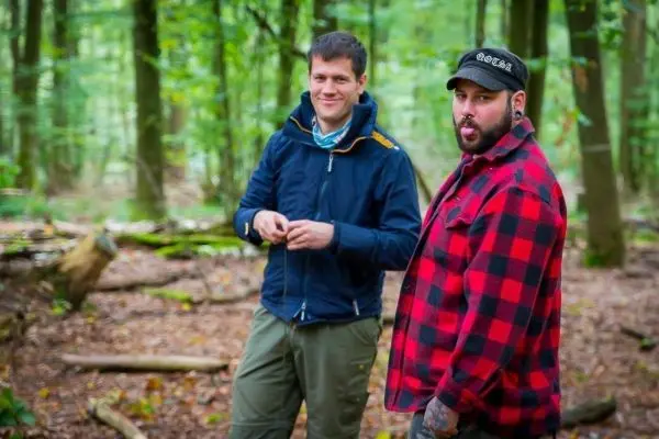 Zwei Personen stehen im Wald und schauen in die Kamera