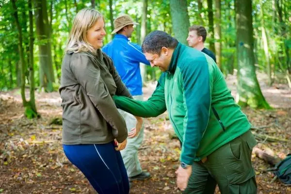Zwei Personen üben eine Technik im Wald, während andere im Hintergrund stehen