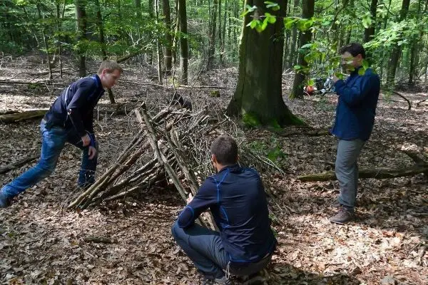 Drei Personen bauen eine Holzunterkunft aus Ästen im Wald