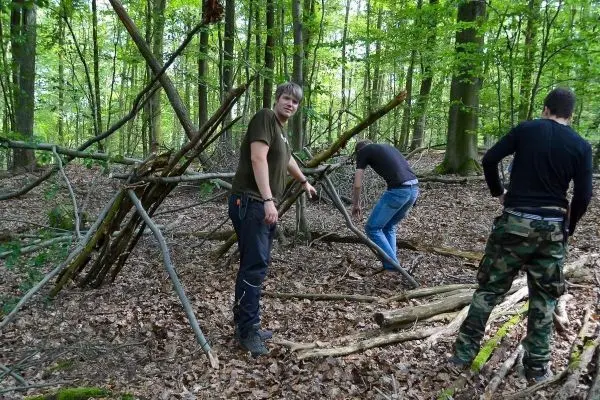 Drei Personen bauen eine improvisierte Unterkunft aus Ästen im Wald