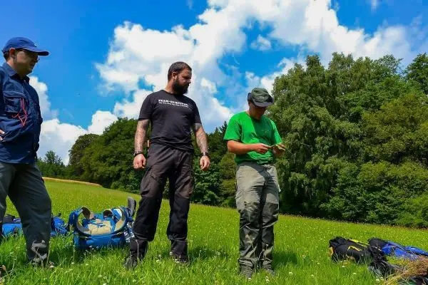 Drei Personen stehen auf einer Wiese und betrachten eine Karte beim Überlebenstraining