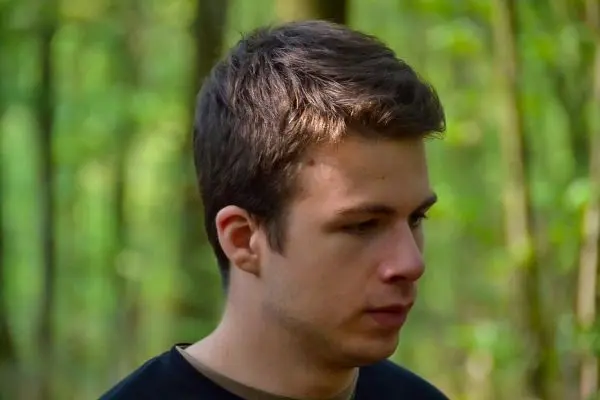 Ein junger Mann steht im Wald und schaut nachdenklich zur Seite