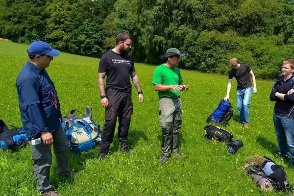 Fünf Personen stehen auf einer Wiese und besprechen Ausrüstungstaschen
