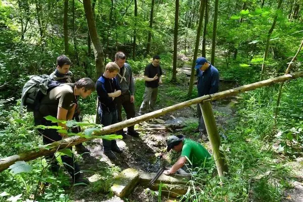 Gruppe beobachtet eine Person, die am Wasserlauf arbeitet