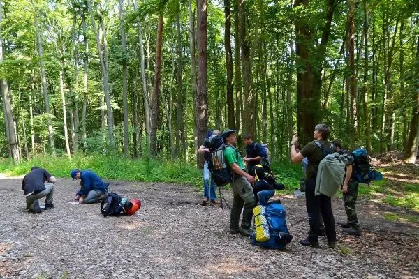 Gruppe mit Rucksäcken steht im Wald, einige knien am Boden