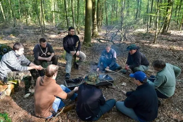Gruppe sitzt um ein kleines Feuer im Wald und bereitet Essen zu