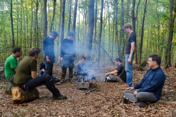 Gruppe sitzt um einen Hobo-Kocher mit Rauchentwicklung im Wald