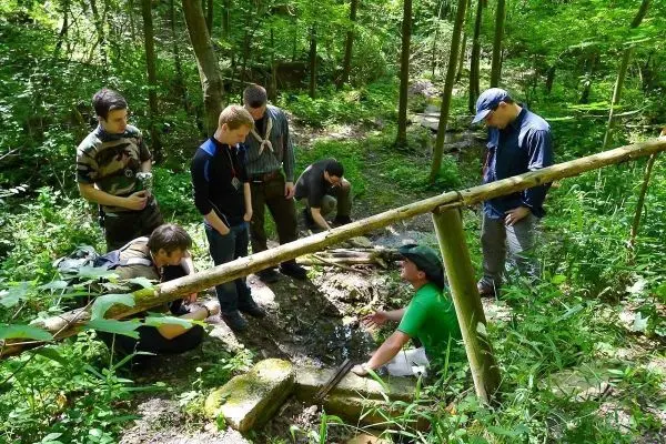 Gruppe um einen Wasserlauf versammelt, einer zeigt Wasseraufbereitungstechniken