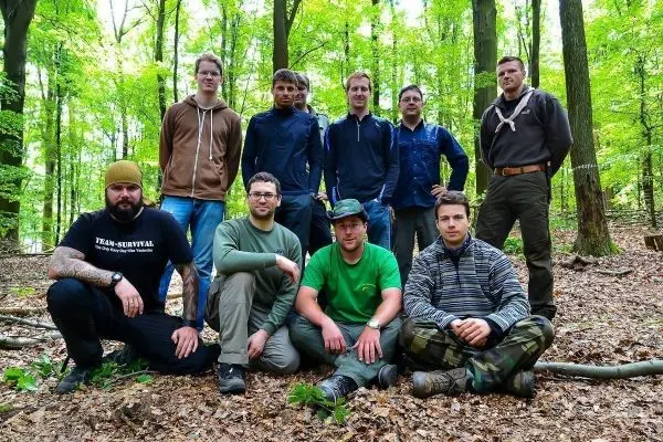 Gruppe von acht Personen sitzt und steht im Wald zwischen Bäumen und Laub