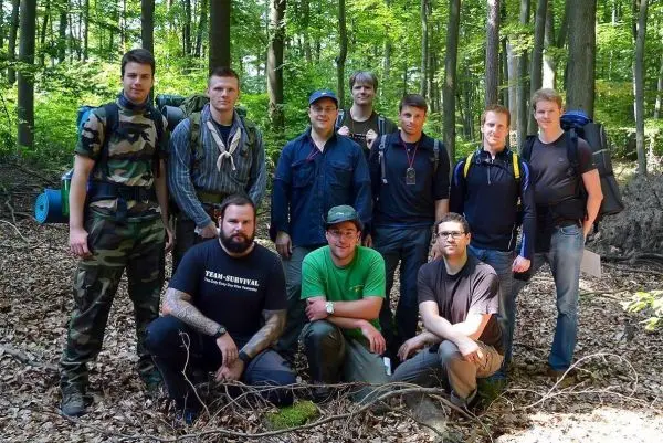 Gruppe von zehn Personen in Waldlandschaft, einige tragen Rucksäcke und Outdoor-Bekleidung