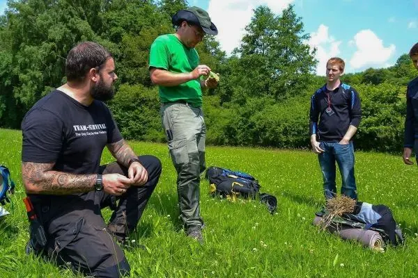 Gruppierung von Personen auf einer Wiese mit Rucksäcken und Ausrüstung