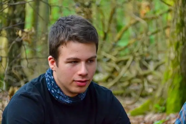 Junger Mann sitzt im Wald, umgeben von Bäumen und Sträuchern