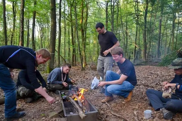 Kleine Flamme brennt in einer Feuerstelle, während mehrere Personen umherstehen