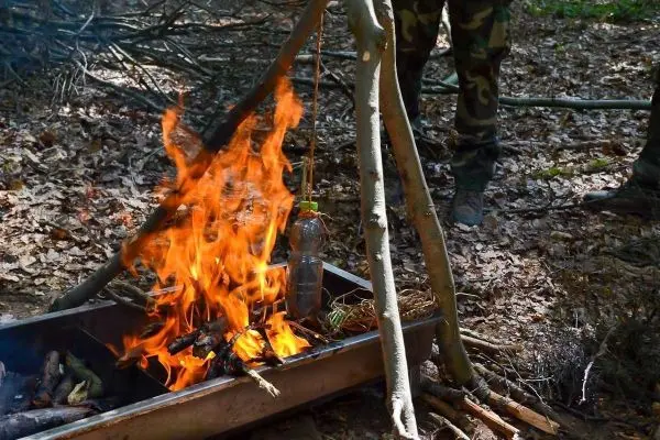 Kleine Flamme brennt in improvisiertem Feuerplatz mit Wasserflasche