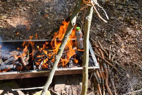 Kleine Flamme kocht Wasser in einer hängenden Flasche über einem Feuer