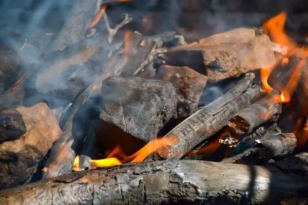 Kleine Flamme zwischen Holzstücken, Rauch steigt auf