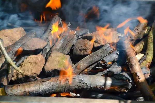 Kleine Flamme zwischen Holzstücken und Steinen, Rauch steigt auf