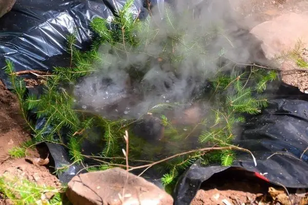 Kleines Bodenfeuer unter Tannenzweigen auf schwarzer Folie erzeugt Rauch