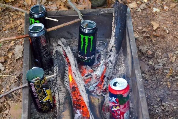 Kohle glüht zwischen Holzstücken in einer Feuerstelle mit Getränkedosen