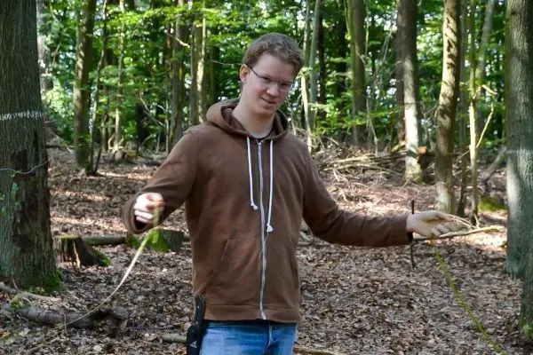 Mann hält ein Seil in der Hand und zeigt auf eine selbstgebaute Seilquerung