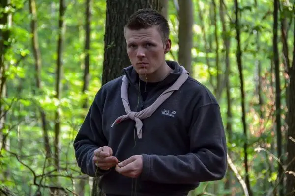 Mann hält einen kleinen Stock in der Hand, umgeben von Bäumen im Wald