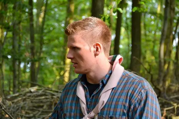 Mann mit kariertem Hemd und Halstuch steht im Wald