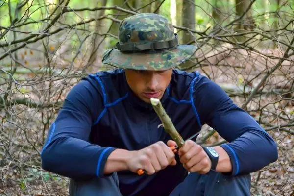 Mann schnitzt mit einem Messer an einem Stock im Wald