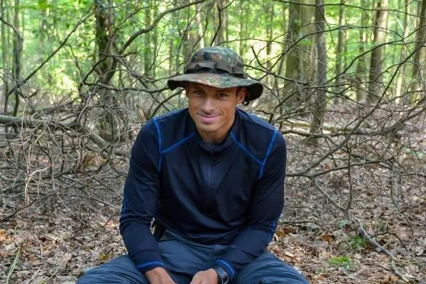 Mann sitzt auf dem Boden im Wald, umgeben von Ästen und Laub