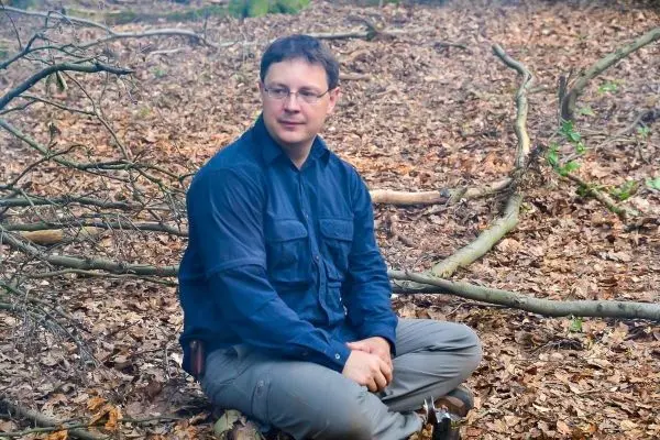 Mann sitzt auf dem Boden im Wald zwischen Laub und Ästen
