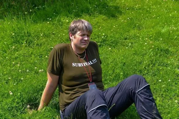 Mann sitzt auf grünem Gras, trägt ein T-Shirt mit Aufschrift und schaut nachdenklich